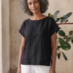 Mujer vistiendo moda atemporal con blusa de lino negro y pantalon de lino blanco