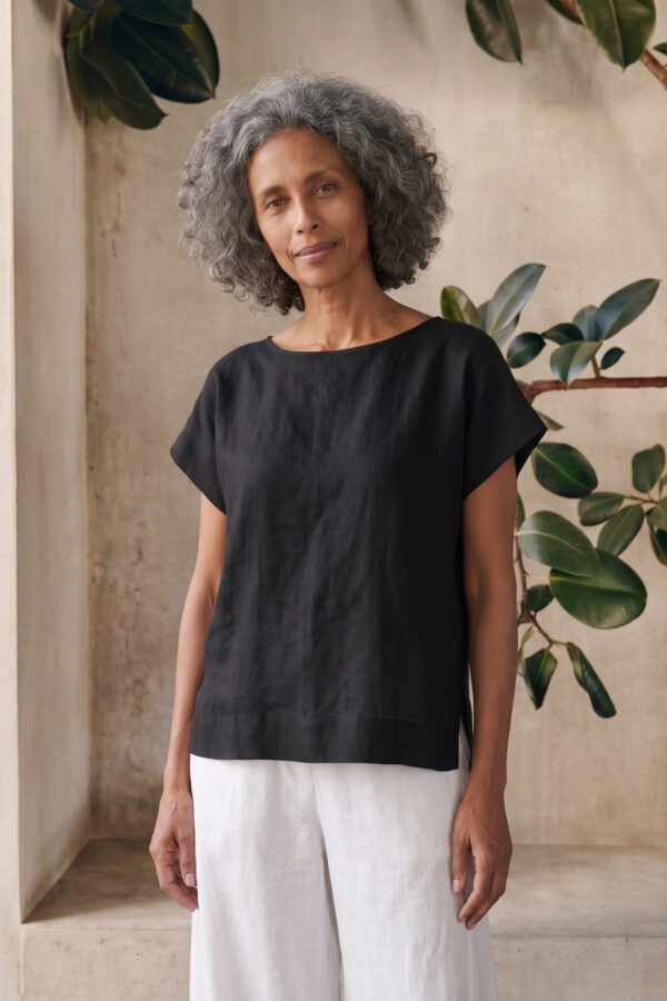 Mujer vistiendo moda atemporal con blusa de lino negro y pantalon de lino blanco