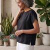 Mujer vistiendo moda atemporal con blusa de lino negro y pantalon de lino blanco