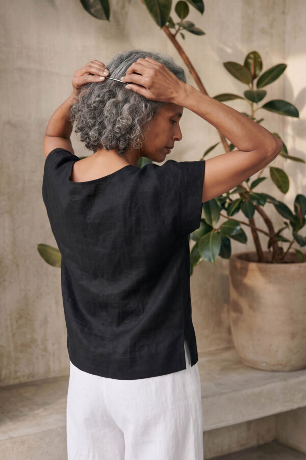 Mujer vistiendo moda atemporal con blusa de lino negro y pantalon de lino blanco