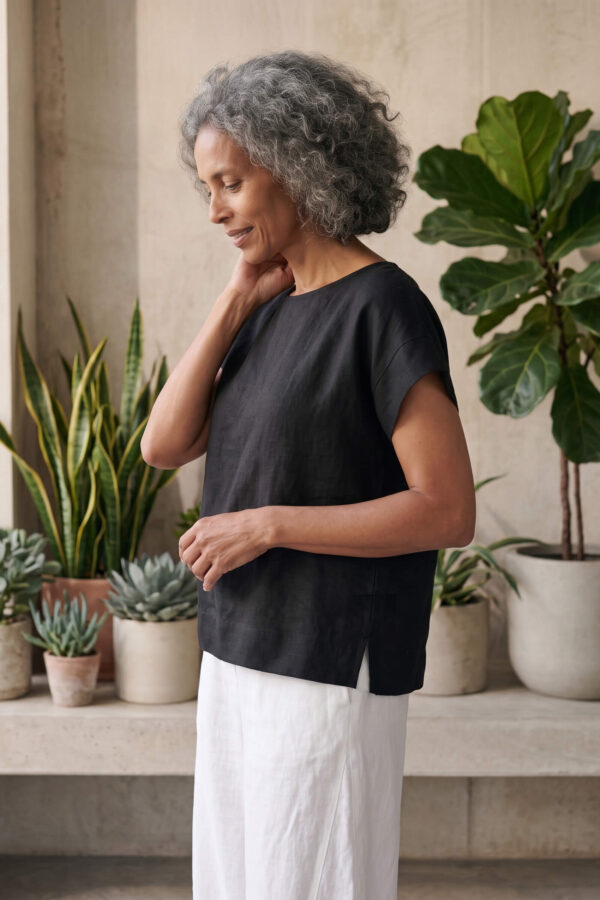 Mujer vistiendo moda atemporal con blusa de lino negro y pantalon de lino blanco
