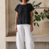Mujer vistiendo moda atemporal con blusa de lino negro y pantalon de lino blanco