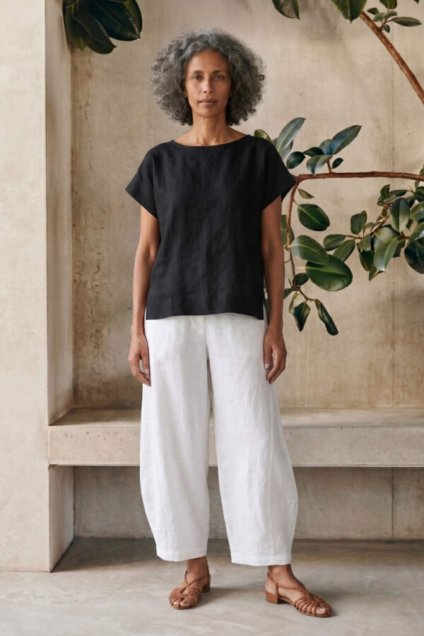 Mujer vistiendo moda atemporal con blusa de lino negro y pantalon de lino blanco