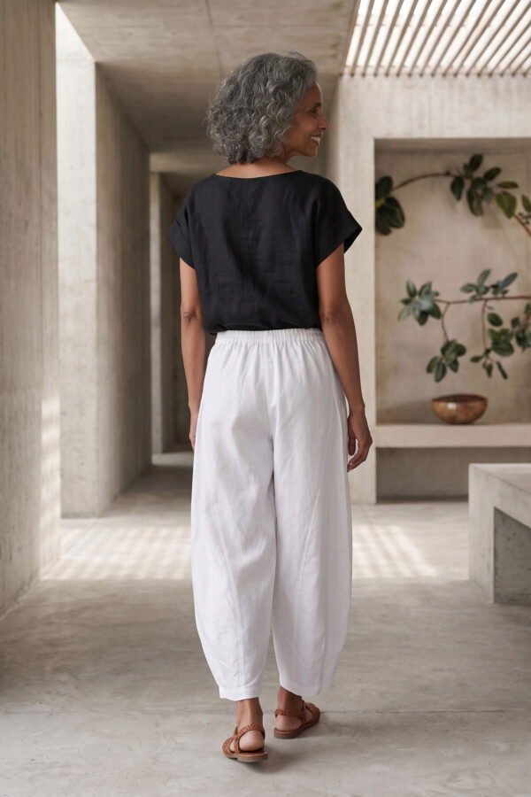 Mujer vistiendo moda atemporal con blusa de lino negro y pantalon de lino blanco